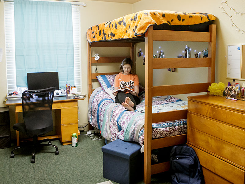 A student sits on the bottom bunk bed and reads a book in a dorm room in Stout. 