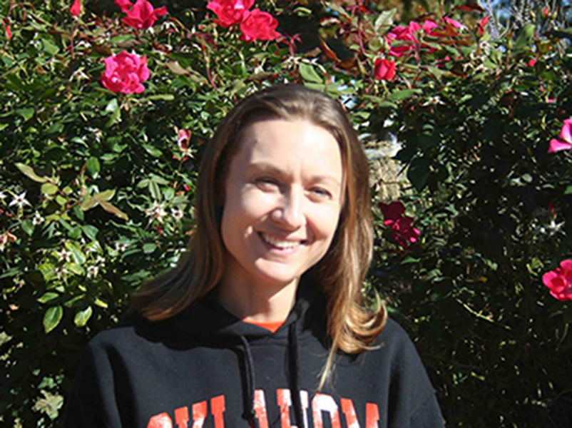 Shelley Schauer, the Honors administrative assistant, smiles for a portrait in front of a rosebush.